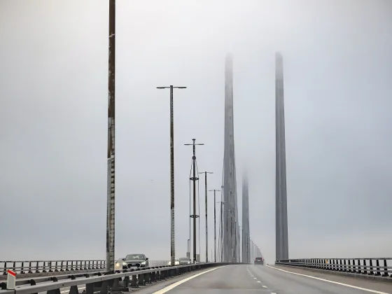 Højbroens kørebane i tåge, begge pyloner forsvinder op i skyen.