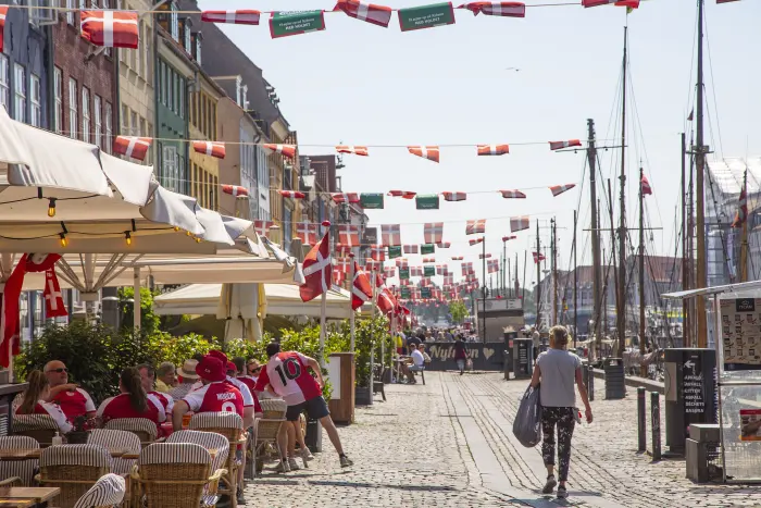 Nyhavn à Copenhague : maisons à pignons colorées, bateaux en bois le long du quai, clients en terrasse.